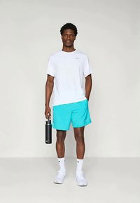 Muška atletska odjeća koja se sastoji od bijele majice kratkih rukava branda Nike, tirkiznih šortseva, bijelih čarapa i crne boce za vodu s Nike logom.