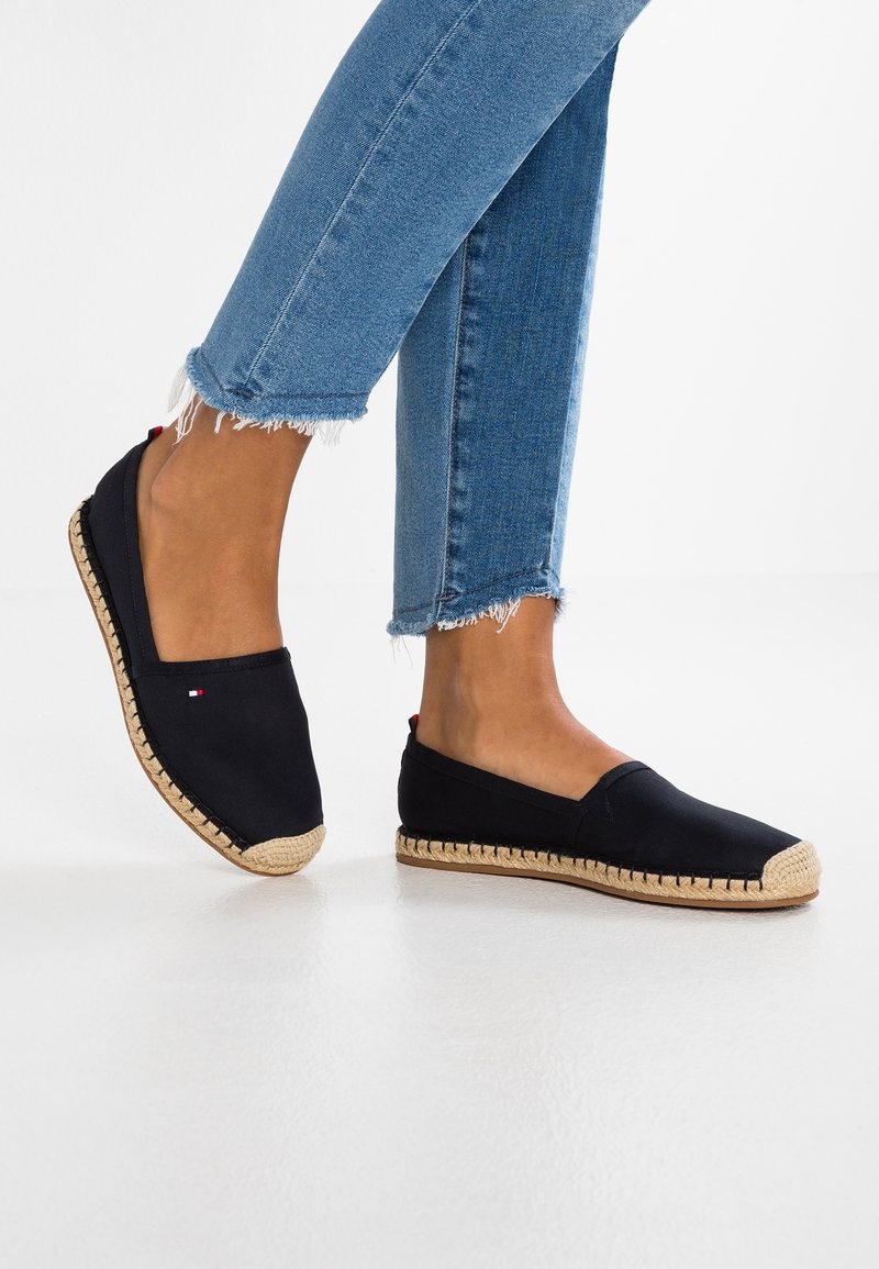 Espadrilles en toile noire avec une semelle en jute tressé et une base en caoutchouc. Design simple à enfiler, avec un petit détail de logo rouge et blanc.