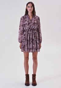 Abito a maniche lunghe, lungo fino al ginocchio, in un motivo paisley malva, con vita cin cin e gonna plissettata. Stivaletti neri marroni.