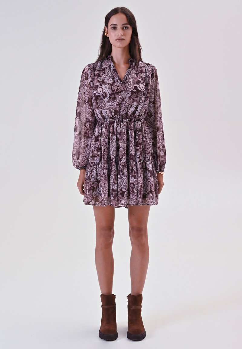 Abito a maniche lunghe, lungo fino al ginocchio, in un motivo paisley malva, con vita cin cin e gonna plissettata. Stivaletti neri marroni.