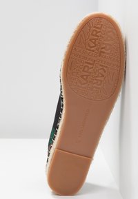 Semelle de chaussure avec le logo KARL LAGERFELD embossé sur du caoutchouc marron clair, détail de bord surpiqué et dessus à motif floral visible.