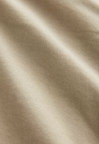 Beige puuvillakangas, jossa on sileä pinta, hienovaraiset raidat ja pehmeä kiilto, esittelee lempeitä taitoksia ja kaaria.