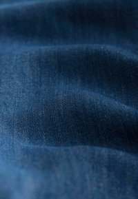 Tumši zila džinsa auduma ar gludu tekstūru, ar smalkām toņu variācijām un redzamu pinuma rakstu.