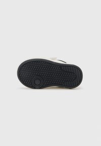 Semelle en caoutchouc noir d'une sneaker blanche arborant la marque Calvin Klein Jeans et un marquage de taille 20 sur un fond blanc uni.