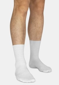 Weiße Baumwollsocken mit geripptem Muster und knöchellangem Design, angezeigt an nackten Beinen mit einem glatten Hautbild.