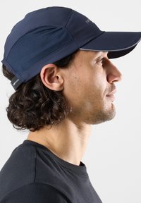 Cappellino blu navy con visiera curva, realizzato in tessuto leggero. Pannelli in rete sui lati per la ventilazione e cinturino regolabile sul retro.