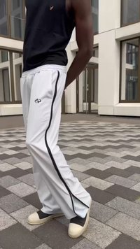 Bijele sportske hlače s crnim bočnim trakama i detaljima na zipu, u kombinaciji s bež i tamnim cipelama. Nosene su s crnim bezrukavnim topom.