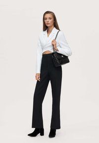 White cropped blazer, high-waisted black trousers, and black ankle boots. Model holds a quilted black handbag with a chain strap.