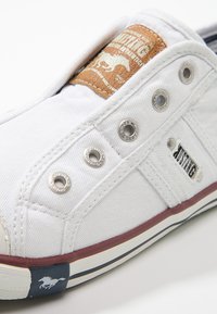 Weiße Leinenschlupfschuhe mit silbernen Ösen, braunem Lederetikett und rotem Akzent. Mit einer Gummisohle, die einen blauen Streifen und ein Logo hat.