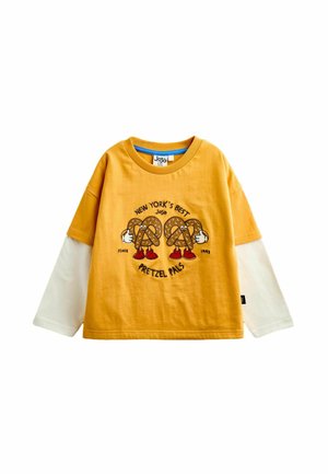Geel-wit kinder shirt met lange mouwen met cartoon pretzels, rode schoenen en tekst "New York's Best Pretzel Pals" op de voorkant.