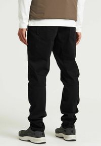 Pantalones negros de diseño recto, fabricados con tela duradera, que cuentan con bolsillos traseros y un ligero ajuste en los tobillos, combinados con zapatillas grises.