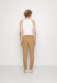 Pantaloni jogger bej cu un croi conic, betelie elastică și tivuri manșonate, purtați cu un top alb fără mâneci. Textură netedă a țesăturii.