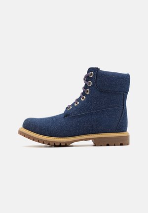 Bottes de cheville en tissu bleu avec une finition texturée, bout rond et semelle en caoutchouc beige. Présente des œillets en métal et des lacets foncés.
