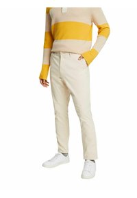 Chinos beige in cotone con vestibilità slim, dotati di chiusura a bottoni e tasche frontali, abbinati a sneakers bianche e un maglione a righe.