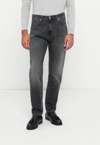 Graue Denim-Jeans mit geradem Schnitt, ausgestattet mit fünf Taschen, einem Knopfverschluss und dezenten Verwaschungen; getragen mit schwarzen Lederschuhen.