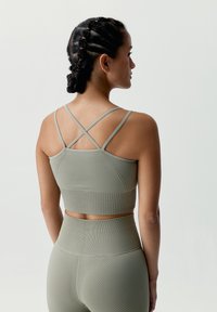 Olivově zelená sportovní podprsenka s texturovaným žebrovaným designem, se zkříženými ramínky vzadu a zkrácenou délkou.