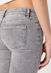 Pantalones vaqueros gris de denim con un ajuste slim, que cuentan con un diseño clásico de cinco bolsillos, una textura sutil y un bolsillo trasero ligeramente desgastado.