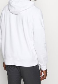 Witte hoodie gemaakt van zachte stof, met een relaxte pasvorm en geribbelde boorden aan de mouwen en tailleband. Eenvoudig ontwerp, zonder patronen.