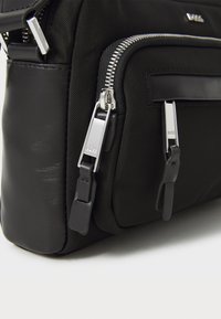 Black nylon bag featuring silver zippers and leather accents, with two zippered pockets on the front for additional storage.