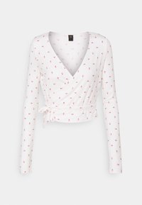 Bílý dlouhý rukávový zavinovací top s hlubokým V výstřihem, zdobený malým růžovým květinovým vzorem a vázáním v pase. Měkká, ribsovaná textura.