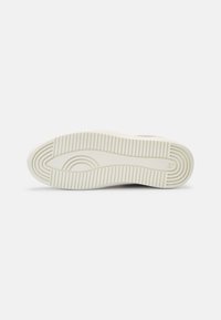 Semelle d'une basket blanche avec des motifs de bande de roulement rainurés et des dessins circulaires concentriques au niveau des orteils et du talon.
