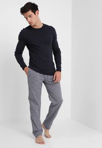 Camisa de manga larga azul marino combinada con pantalones de pijama a cuadros grises. Tela suave, corte ajustado y detalles lisos en la camisa. Sin calzado.