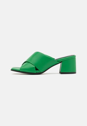 Mule sandale verte à bout ouvert avec de larges brides croisées et un talon bloc, présentée sur un fond blanc.