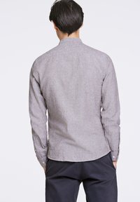 Camicia a maniche lunghe grigia chiara con tessuto testurizzato, polsini abbottonati e orlo curvo. Design minimalista con scollatura senza colletto.