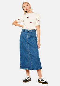 Baltas megztinis su raudonom vyšnių siuvinėjimais, derinamas su mėlynu džinsiniu maksi sijonu. Modelis dėvi juodus ir baltus sportbačius.