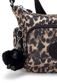 Leopard print crossbody bag with black accents, featuring a zippered pocket, silver hardware, and a black gorilla charm. Textured fabric.