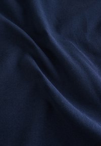 Tissu bleu foncé avec des plis doux et une surface légèrement texturée sous un éclairage naturel.