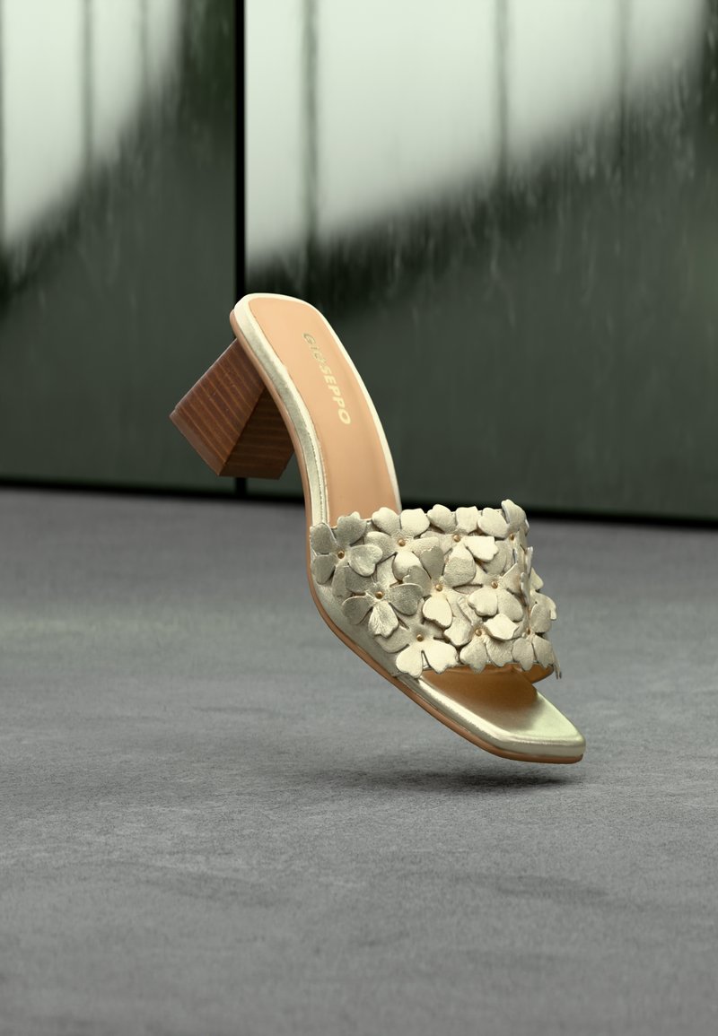 Μπεζ σανδάλι με τακούνι πλατφόρμα και λουρί διακοσμημένο με τρισδιάστατες εφαρμογές λουλουδιών σε γκρι επιφάνεια.