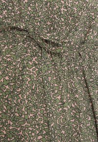 Robe à motif floral en tissu rose clair avec des formes abstraites vertes. Dotée d'une taille froncée et de plis, créant un effet texturé.