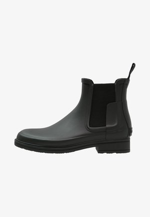 Bottines Chelsea noires en caoutchouc avec une finition lisse, des panneaux élastiques sur les côtés et une languette. Elles présentent un petit talon carré et un design à bout rond.