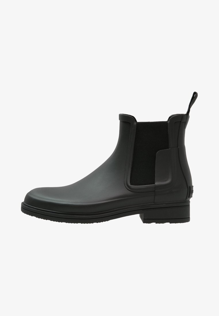 Bottines Chelsea noires en caoutchouc avec une finition lisse, des panneaux élastiques sur les côtés et une languette. Elles présentent un petit talon carré et un design à bout rond.
