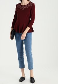 Burgunderfarbenes Peplum-Top mit einer Spitze am Ausschnitt, kombiniert mit hellblauen cropped Jeans und schwarzen Slippers.