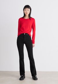 Suéter rojo de manga larga combinado con jeans negros de talle alto. Los jeans tienen un corte ajustado y están complementados con zapatos de plataforma negros.