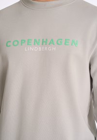 Sudadera gris claro con texto impreso en verde y blanco "COPENHAGUE LINDBERGH." Textura suave con cuello redondo.