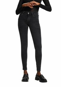 Mustat farkut slim fit -mallilla, viidellä taskulla, nappisuljenta ja tyylikäs muotoilu, yhdistettynä mustiin loafer-kengiin, jotka korostavat sileää pintaa.