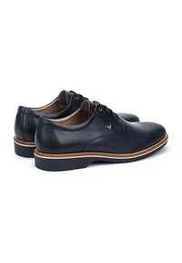Chaussures en cuir noir avec une texture lisse, bout rond et coutures accentuées en marron. Conçues avec un petit talon et un système de laçage classique.
