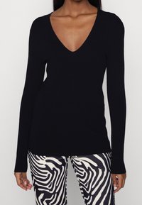 Schwarzes langärmliges V-Ausschnitt-Oberteil, geripptes Textil, figurbetontes Design. Kombiniert mit Hosen im Zebra-Print, die einen gewagten Mustermix schaffen.