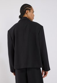 Zwarte oversized blazer met gestructureerde schouders, een gladde textuur en een minimalistisch ontwerp. Beschikt over een enkele achternaad en brede mouwen.