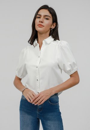 Hvit bluse med pufferm, knappelukking foran, krage og elastiske mansjetter. Kombinert med tettsittende blå denimjeans.