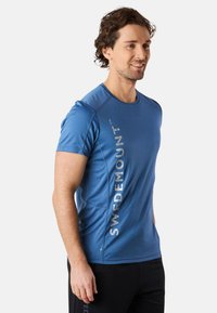 kortärmad blå atletisk tröja i slät tyg, med en vertikal "SWEDEMOUNT"-logotyp i silver på vänster sida.