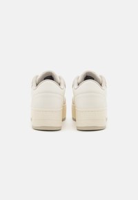 Vita läderskor med låg design, texturerade detaljer och en tjock krämfärgad sula. Har en vadderad krage för komfort.