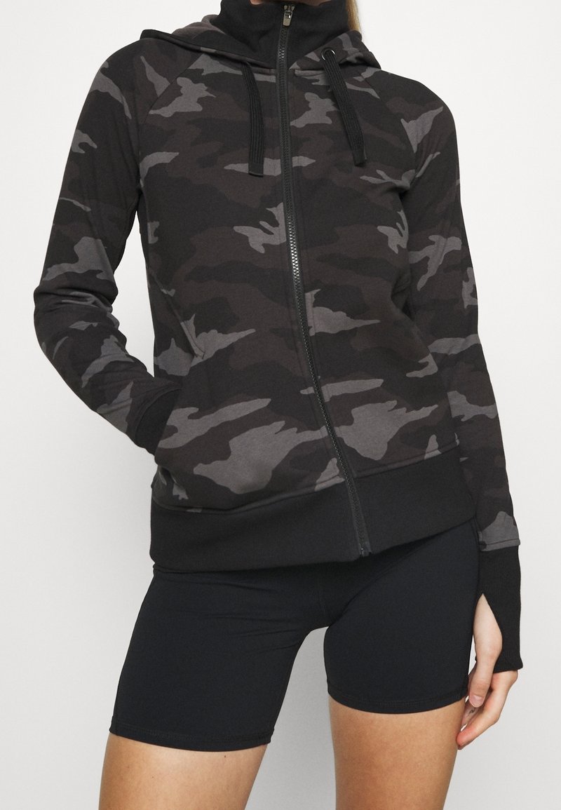 Haut de hoodie zippé noir camouflage avec un haut col, des manches longues et des poignets côtelés. Fait d'un tissu doux et flexible.