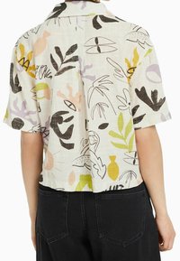 Korte mouwen blouse met kraag van lichtgewicht stof, met een gekleurd abstract patroon met bladeren en vormen op een crèmekleurige achtergrond.