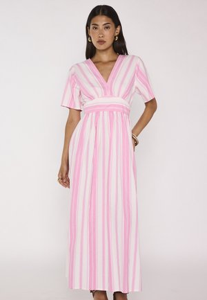 Donna che indossa un vestito lungo a righe rosa e bianche con scollo a V, maniche corte e orecchini a cerchio dorati su uno sfondo chiaro uniforme.
