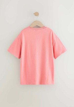 T-shirt en coton rose suspendu à un cintre en bois, mettant en avant un col rond et des manches courtes, avec une texture lisse et une coupe décontractée.