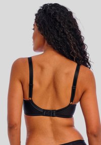 Sujetador negro con tirantes ajustables y cierre de gancho. Tejido texturizado con sutiles rayas verticales. Presenta un acabado suave y elegante.